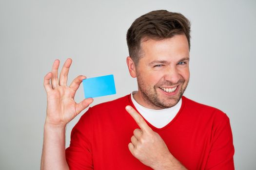 Portrait of amazed smiling young man holding credit card. Studio shot