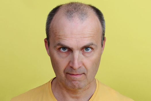 Close-up face of a handsome middle-aged man in a yellow undershirt. Portrait of a handsome man 45-55 years old on a yellow background.