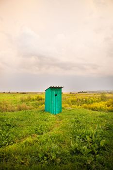 wooden toilet with a carved window in the shape of a heart, an open field.