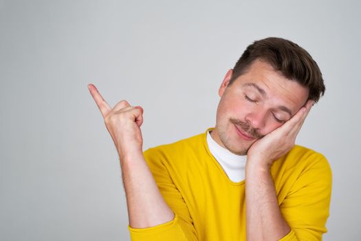 Tired and sleepy guy leaning on palm, closing eyes and sleeping pointing aside.