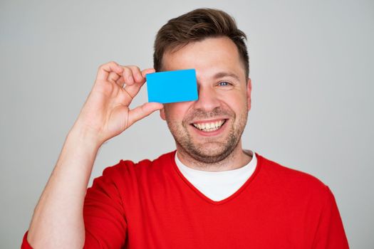 Portrait of amazed smiling young man holding credit card. Studio shot