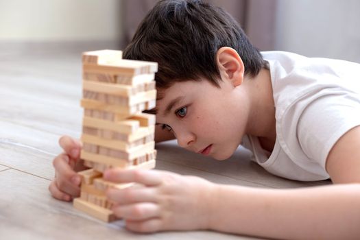 Portrait of the boy lie on the floor and play the game of tower wood blocks . Family board games