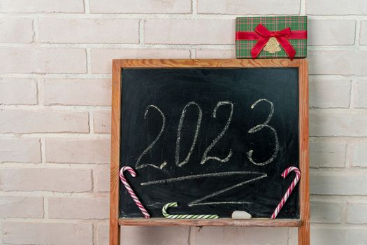 a black slate decorated with candy in the form of a caramel cane. The year 2023 is written in chalk on the blackboard. Happy New Year. 2023. Number written in chalk on a school board