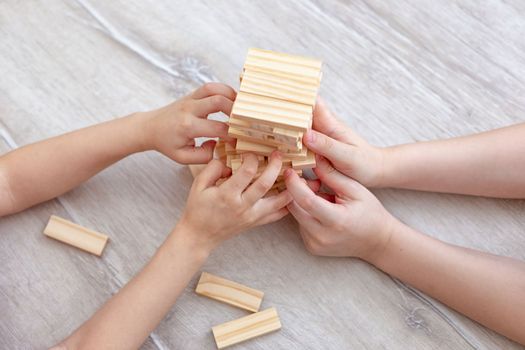 Four Childrens hands collects a tower of wooden blocks on the floor. Close up. Family board games