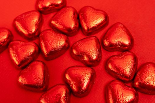 lots of heart-shaped candies wrapped in red foil on a red background. A declaration of love. a gift and gratitude. Valentine's Day. postcard.