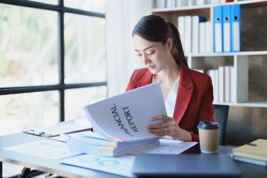 Portrait of a thoughtful Asian businesswoman looking at financial statements and making marketing plans using a computer on her desk.