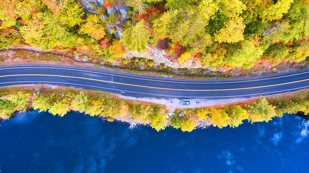 Image of Aerial looking down on road between blue water lake and rocky forest in fall