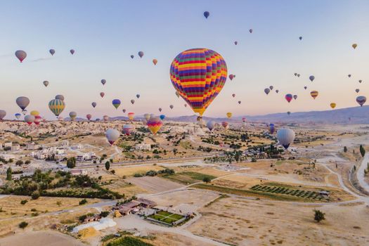 Colorful hot air balloons flying over at fairy chimneys valley in Nevsehir, Goreme, Cappadocia Turkey. Spectacular panoramic drone view of the underground city and ballooning tourism. High quality.