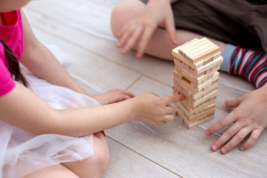 Two Childrens hands collects a tower of wooden blocks on the floor. Close up. Family board games