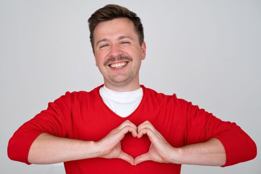 Young handsome man in love doing heart symbol shape with hands. Romantic concept. 