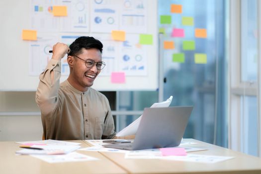 Happy male entrepreneur emotionally celebrating business success with laptop in office.