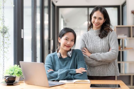 Two young Asian women show joyful expression of success at work smiling happily with a laptop computer in a modern office...