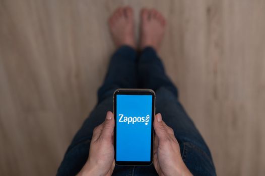 December 3, 2022 Almaty Kazakhstan: Barefoot woman holding smartphone with zappos logo