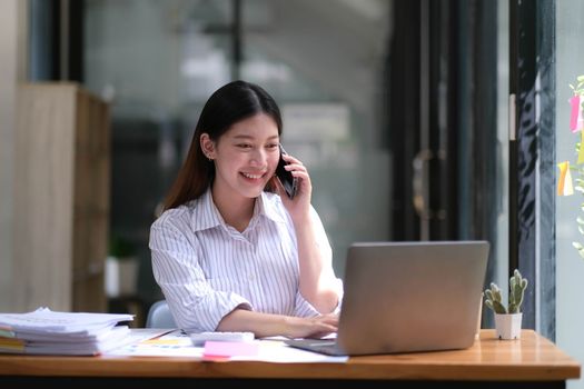 Portrait of young asian business woman talk on smartphone write notebook laptop in home office. Beautiful girl at desk computer take home order. Startup business asia woman online sme telemarketing...