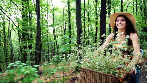 a woman in a hat and dress, with a basket of flowers, together with small child, ride bicycle, in the forest, in the summer. the child is sitting in a special chair. High quality photo