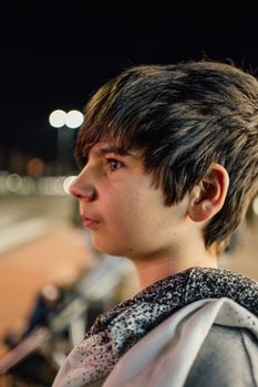 Portrait of caucasian teenager boy at night in the street with burning lights in the background.