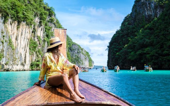 Asian women in front of a longtail boat at Kho Phi Phi Thailand, women in front of a boat at Pileh Lagoon with turqouse colored ocean