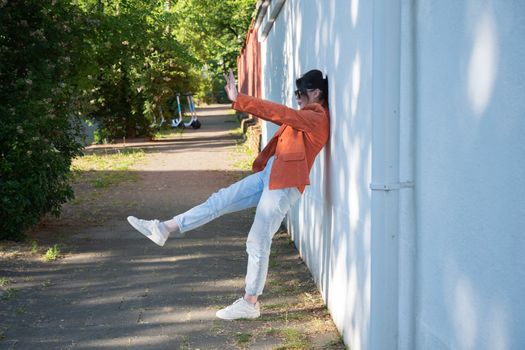 young brunette fooling around near a brick wall in a beautiful red jacket, light and shadow. High quality photo