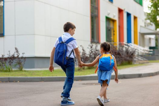 two schoolchildren, a little girl and a boy, brother and sister with backpacks hold hands go to school in the morning on a sunny day. Close up. Mock up