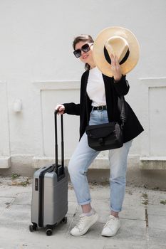 a young brunette in glasses with a suitcase goes on vacation, a woman stands against the background of a beautiful brick wall High quality photo