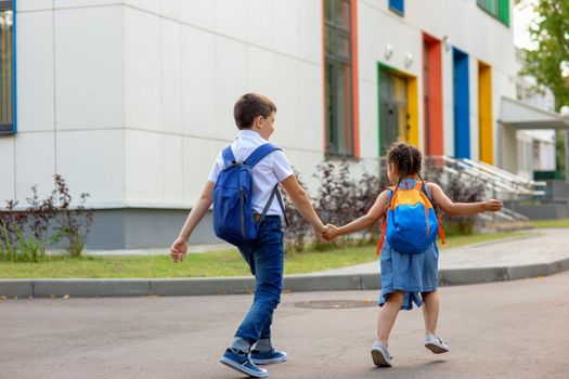 two schoolchildren, a little girl and a boy, brother and sister with backpacks hold hands run to school in the morning on a sunny day. Close up. Mock up