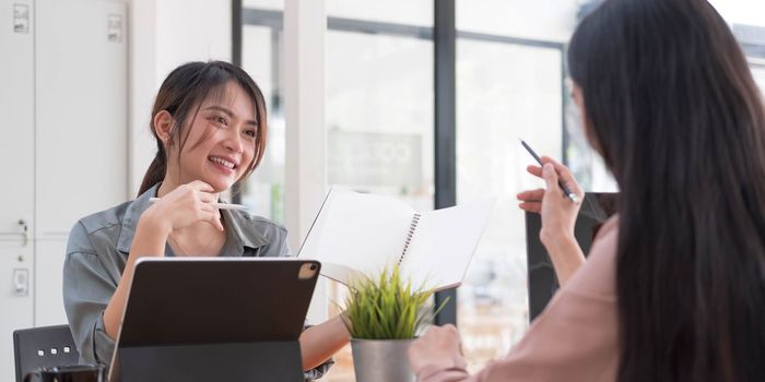 Two young Asian businesswomen show joyful expression of success at work smiling happily with a laptop computer in a modern office...