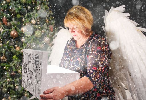 smiling lonely woman opens a christmas present near the christmas tree. Woman with angel wings, Christmas wonder.