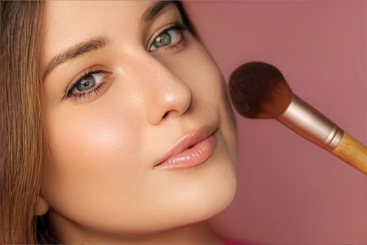 Beautiful young woman applying cosmetic powder product with make-up bamboo brush, beauty, makeup and skincare cosmetics model face portrait on pink background, closeup