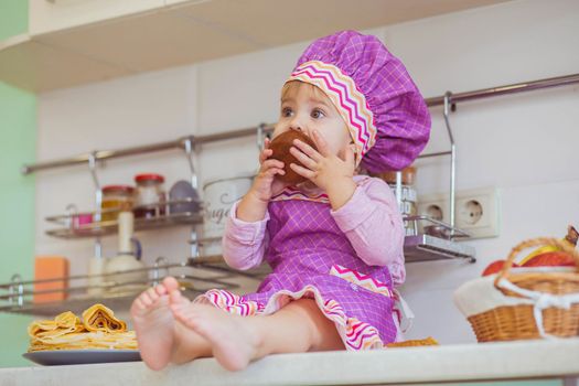 beautiful baby in an apron eating honey on the kitchen table.