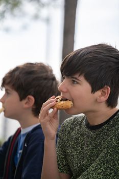 Close up portrait of boys sitting on a bench in park and eating a chocolate biscuit. side view.