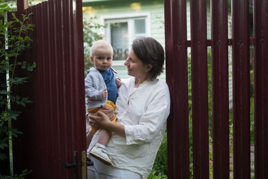Curious woman with a baby opening the gate of fence and looking at camera welcoming friends