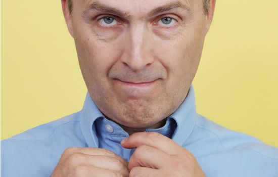 Close up portrait of a casual man buttoning his shirt. A man in a blue shirt on a yellow background.