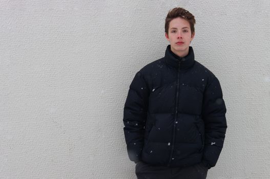 A boy of 14-17 years old stands against the wall and keeps his hands in his pockets.