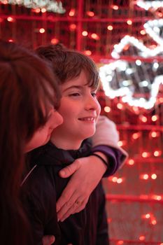 Side view - cute mother and son embrace behind red white lights at night.