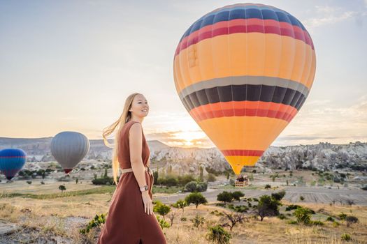 Tourist woman looking at hot air balloons in Cappadocia, Turkey. Happy Travel in Turkey concept. Woman on a mountain top enjoying wonderful view.