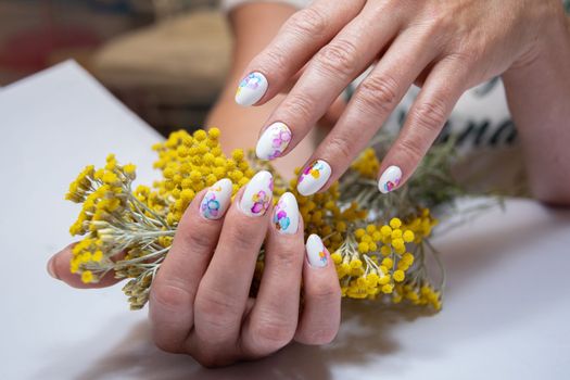 hands with a beautiful multi-colored manicure hold a bouquet of yellow flowers. High quality photo