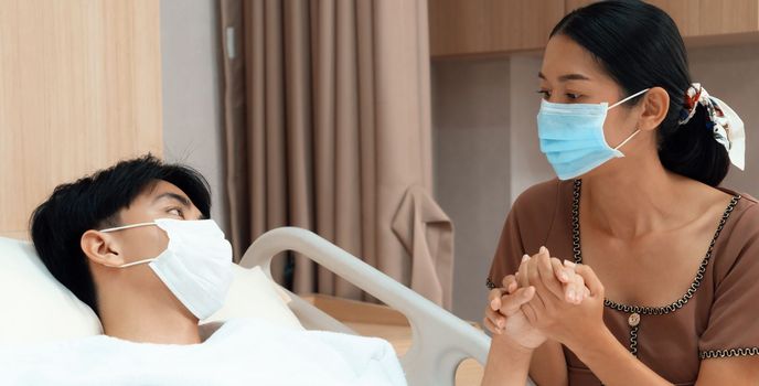 Young patient with attentive visitor and family holding hands in hospital sterile recovery room. The concept of family support for patients receiving hospital care. In-ward medical care and healthcare