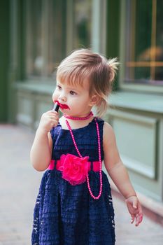 Adorable baby in a dress paints lips with lipstick.