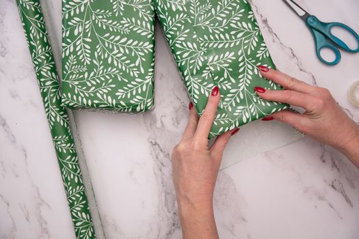 woman's hands with red christmas manicure wrap gifts in green wrapping paper. High quality photo