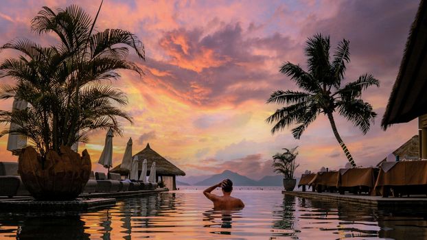 Luxury swimming pool in tropical resort, relaxing holidays in Seychelles islands. La Digue, Young man during sunset by swimpool Seychelles at vacation 