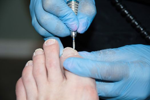 A master in a beauty salon makes a hardware pedicure to a client, Fraser removal of red varnish and cuticles. Close-up, soft focus. High quality photo