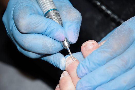 A master in a beauty salon makes a hardware pedicure to a client, Fraser removal of red varnish and cuticles. Close-up, soft focus. High quality photo