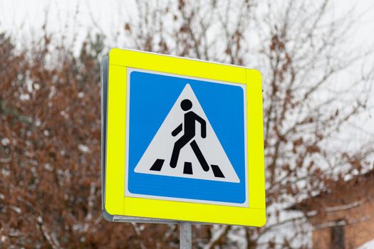 A road sign of a pedestrian crossing in close-up. A sign with a reflective coating is installed on the street and intersection and warns drivers about a pedestrian crossing. Be careful on the road