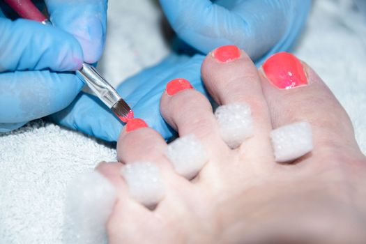 pedicure master paints client's toenails with orange gel polish, foot care in beauty salon, Close-up, soft focus. High quality photo
