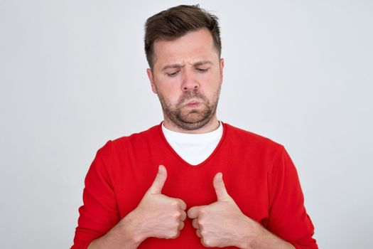 Young man making good thumb up gesture with sad face. Undecided person between yes or not 