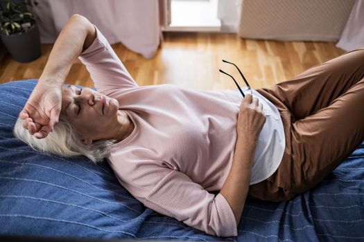 Senior caucasian woman suffering from a headache resting at home on sofa