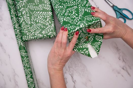 woman's hands with red christmas manicure wrap gifts in green wrapping paper. High quality photo