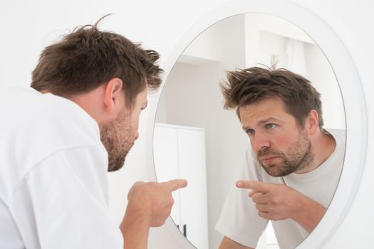 Caucasian mature man trying to encourage himself showing thumb up looking in mirror on the morning.