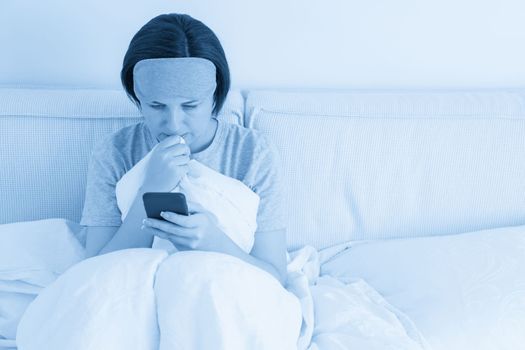 Woman using smartphone as she sits in bed covered with a duvet