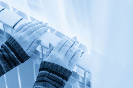 Girl warms up the frozen hands above hot radiator, close up